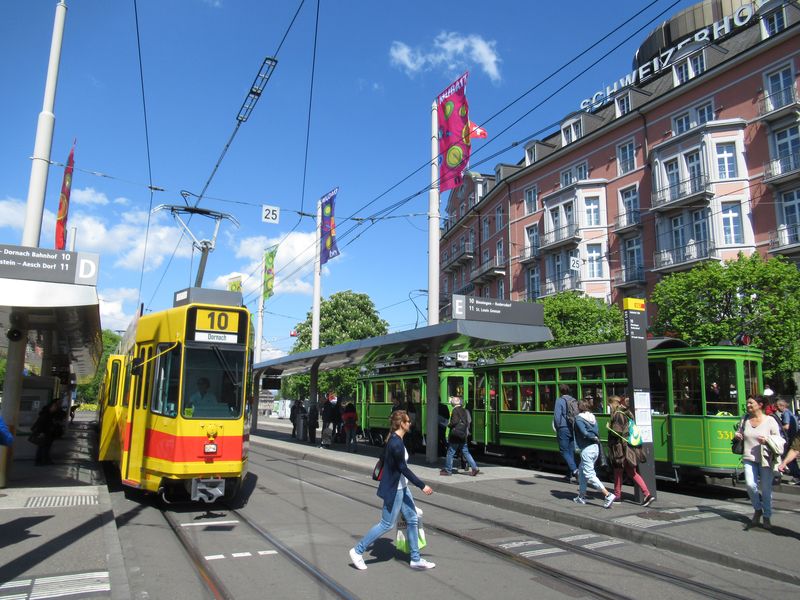 Již pomìrnì raritní situace pøed hlavním nádražím: setkání historické tramvaje urèené pro komerèní využití se starší tramvají pøímìstského dopravce BLT. Tyto dvou- a tøíèlánkové vozy z konce 70. let už úspìšnì nahrazují nové tramvaje Tango od Stadleru. Nejstarší zástupci pùvodních žlutoèervených vozù jezdí už od roku 2016 v srbském Bìlehradu.