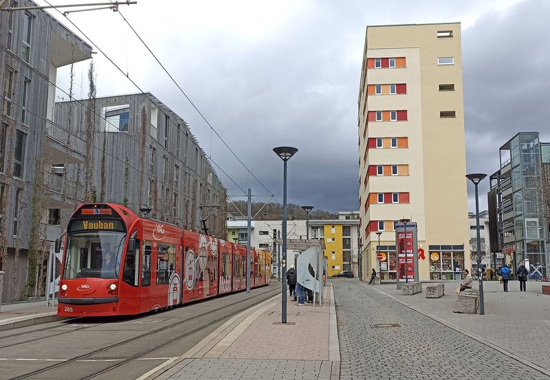 Reklamou polepená tramvaj Siemens Combino uprostøed moderní okrajové ètvrti Vauban na lince 3. Tyto napøíè Evropou typizované tramvaje se ve Freiburgu odlišují výrazným „kšiltem“ pro displej s èíslem linky a koneènou stanicí. Tramvaje sem jezdí od roku 2006.
