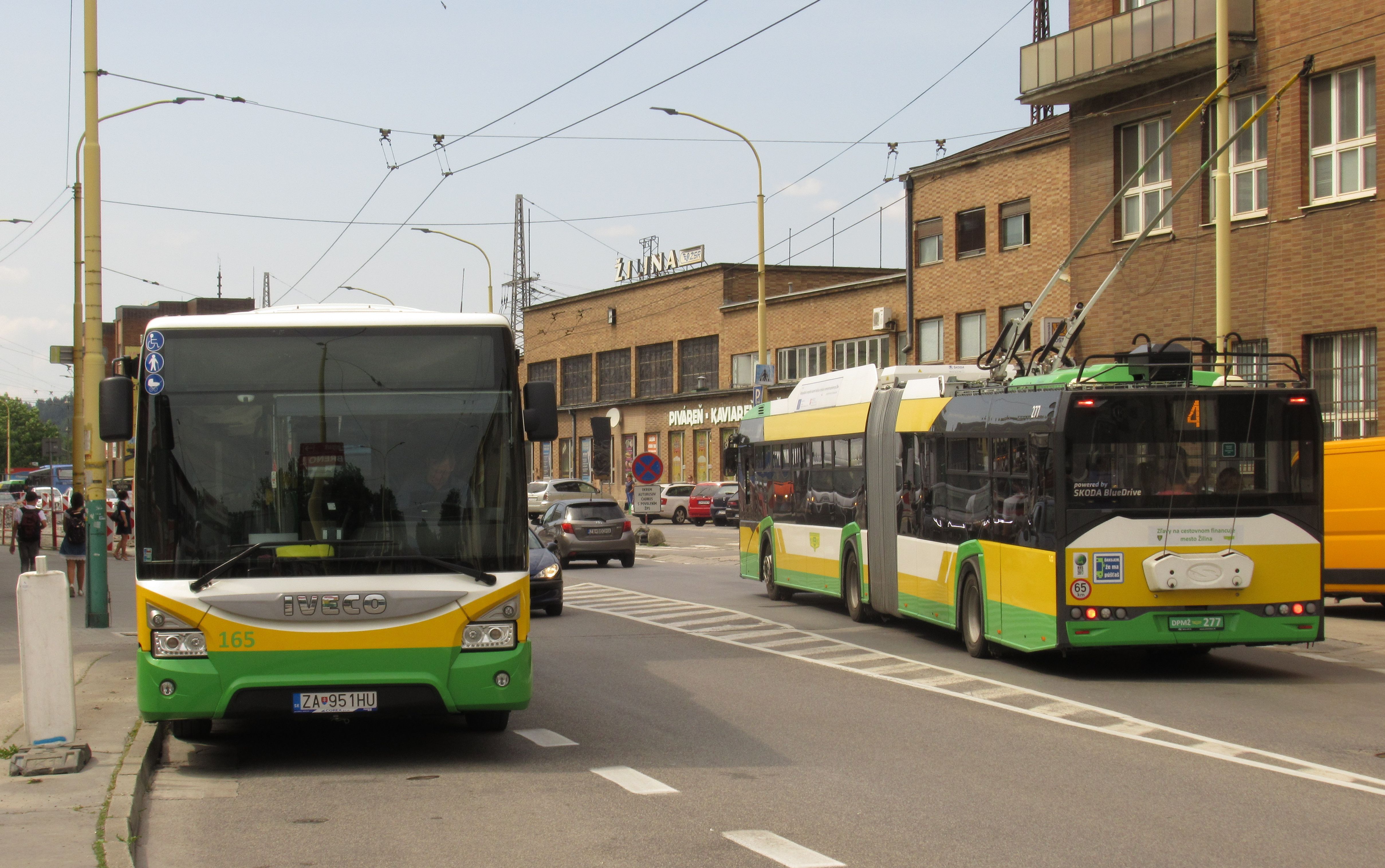 Velká promìna pøed hlavním vlakovým nádražím Žilinì – nový kloubový trolejbus Škoda se potkává s hybridním autobusem Iveco. Radikální obnova vozového parku v posledních letech odtud vyhnala již skoro všechny vysokopodlažní vozy.